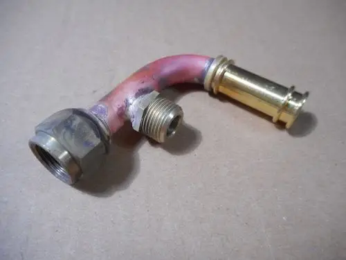 U-förmige Metallverbindung mit verschiedenen Gewinden, möglicherweise für Entlüftungszwecke. Teile aus Messing und einem pinken Rohr, gefertigt von Remeha.